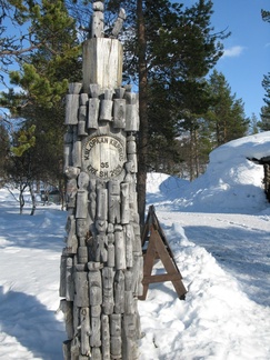 Toteemi pihapiirissä on päällystetty pikku puu-ukoilla. Paalu on muistona erävaelluksen Sm-kisoista vuodelta 2004.